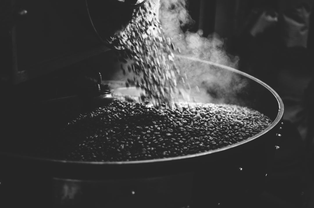 A dark image of fresh roasted coffee beans coming out of the roaster. 