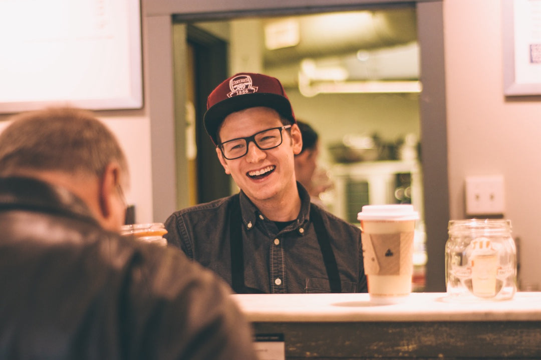 A promotional hiring graphic for Old City Coffee. The background shows a bustling cafe counter where a smiling barista in an apron is actively pulling an espresso shot, highlighting a welcoming and fast-paced work environment.