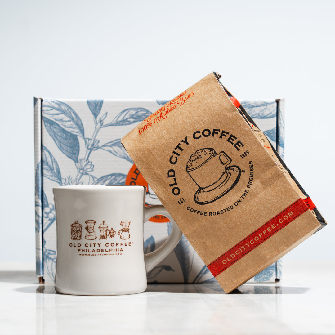 A decorative gift box with its content in front, which includes a branded diner mug and a pound bag of coffee