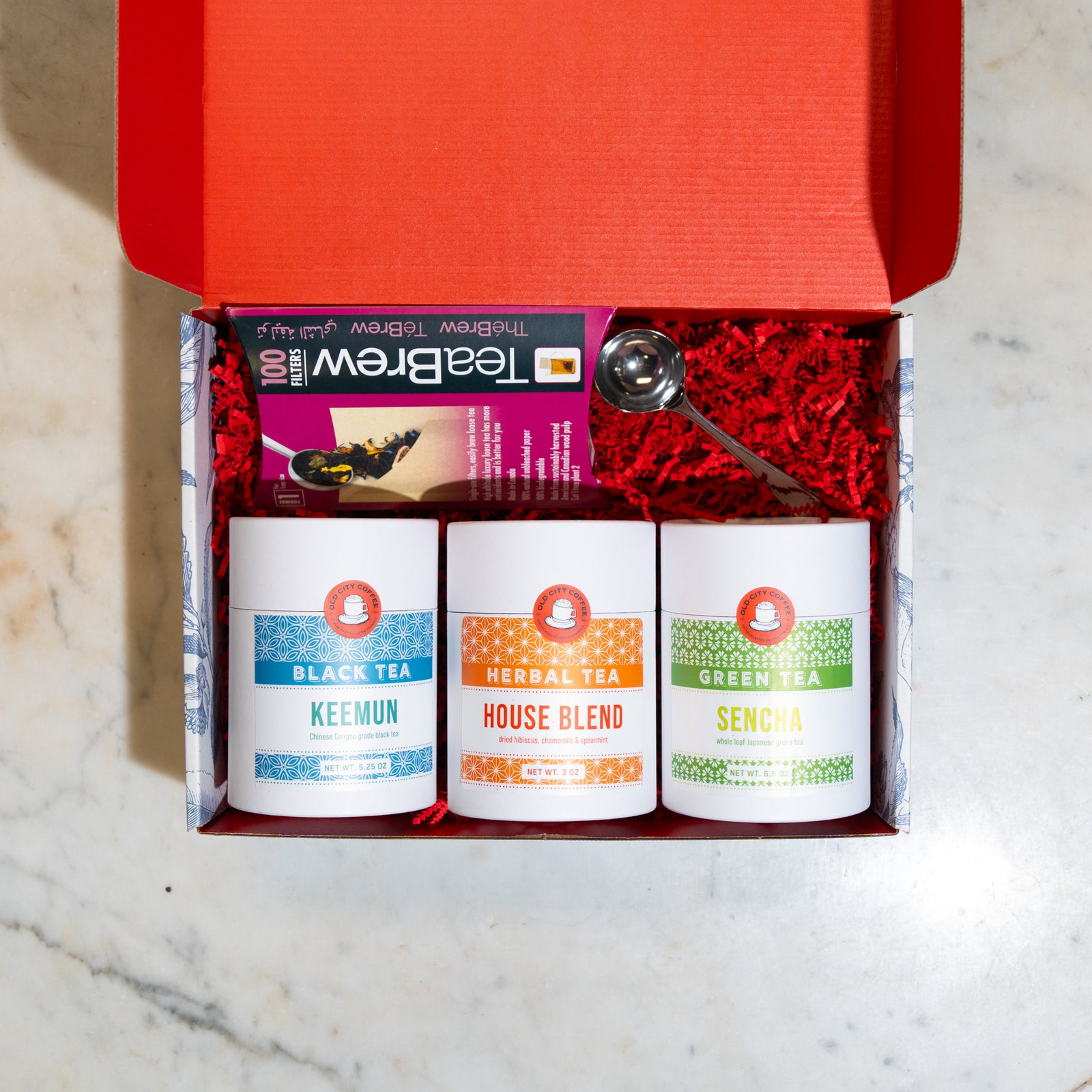Open red gift box with three Old City Coffee tea canisters labeled Keemun, Sencha, and House Blend, plus a box of TeaBrew filters and a stainless tea scoop