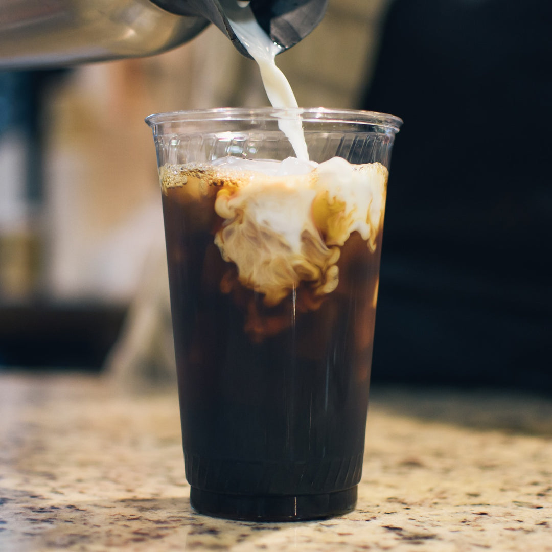 A delicious glass of iced coffee on a granite surface, capturing the moment milk or cream is poured into the cup and begins to swirl into the dark brew.