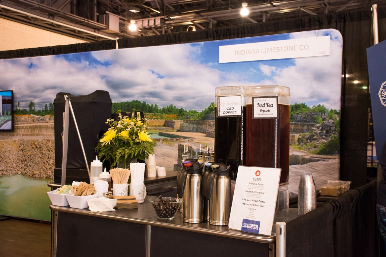 A catered beverage station by Old City Coffee at a convention, showcasing a neat arrangement of hot coffee airpots, iced beverage dispensers, and an organized condiment station with cups, stirrers, and sugar.