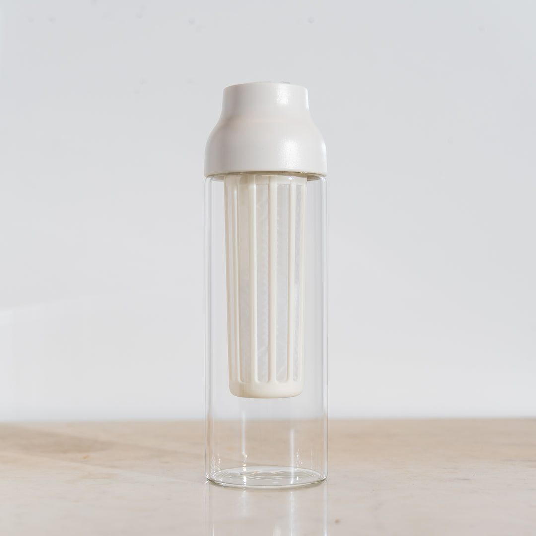 Clear glass bottle with silver lid on a light wooden surface and white background