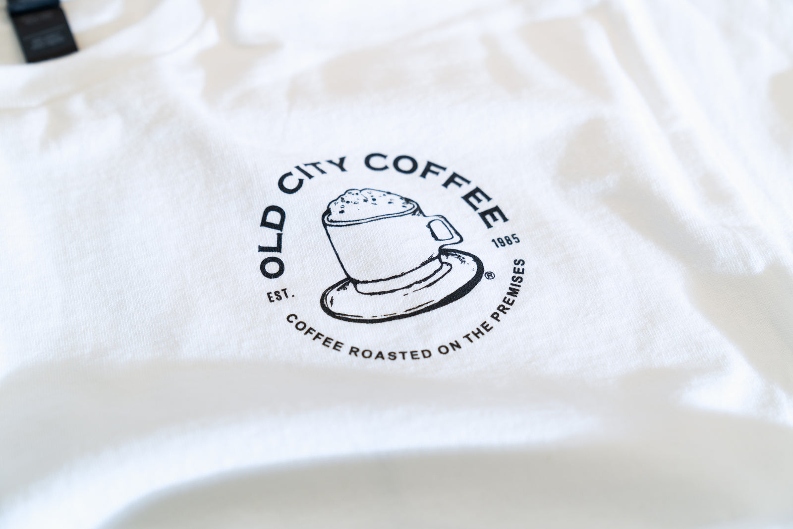 Close-up of the round Old City Coffee logo printed on the white T-shirt