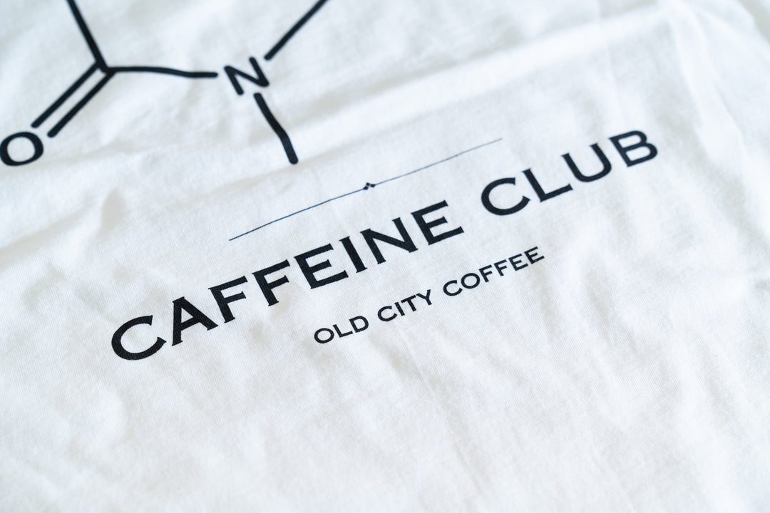 Close-up of the Caffeine Club and Old City Coffee text printed on the white T-shirt