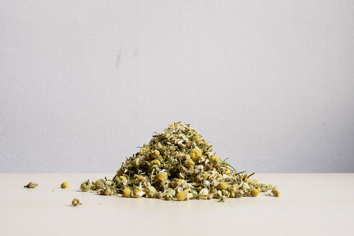 Small pile of dried chamomile flowers on a white surface