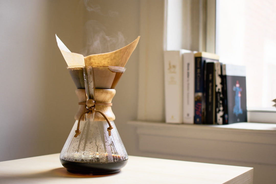 Chemex 10 cup with freshly brewed coffee on a desk beside a row of books