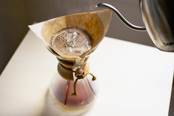 Gooseneck kettle pouring hot water over coffee grounds in the Chemex filter