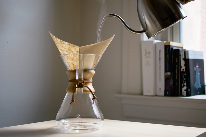 Kettle pouring water into the Chemex paper filter in front of a bookshelf