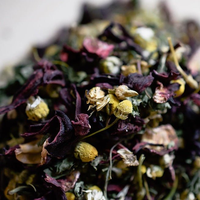 Close-up of loose herbal blend with hibiscus petals, chamomile buds, and green leaves