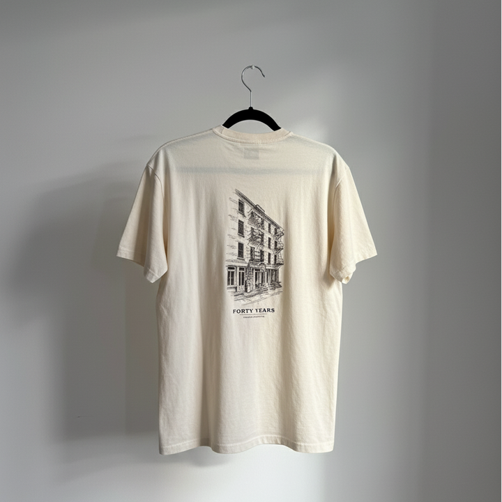 Cream T-shirt on a hanger against a gray wall, showing the storefront illustration back print