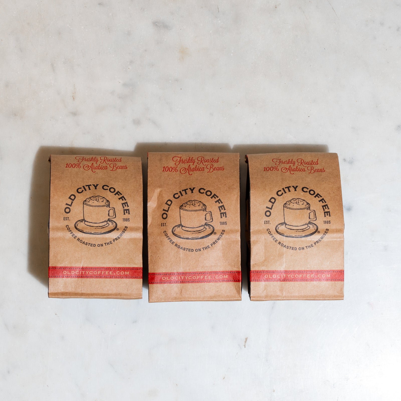 Three kraft Old City Coffee bags standing in a row on a marble counter