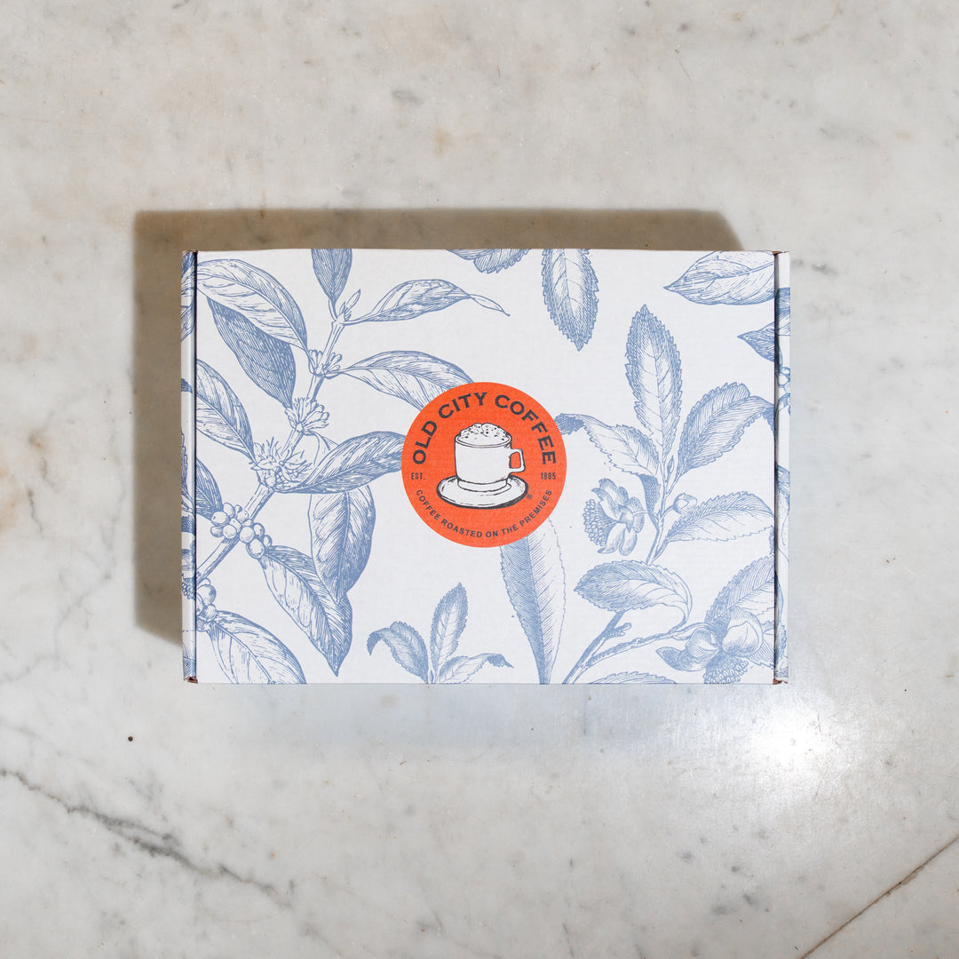 Closed gift box with a blue botanical leaf pattern and a round Old City Coffee logo sticker on the lid