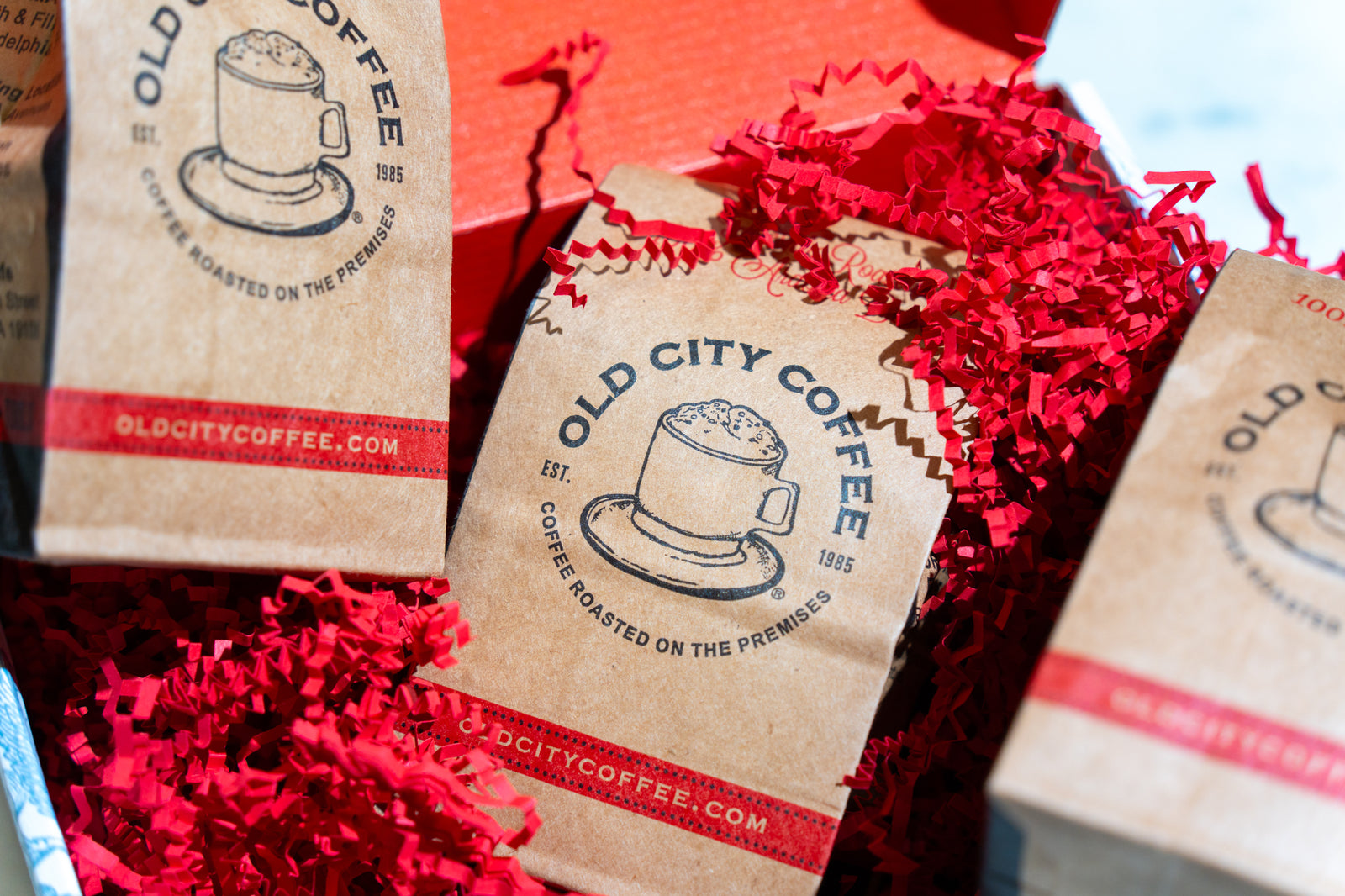 Three kraft Old City Coffee bags nestled in red crinkle paper inside a gift box