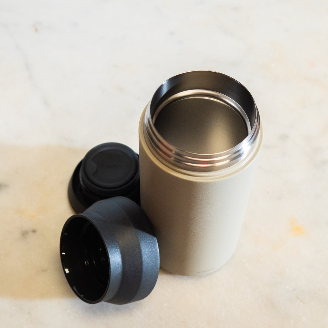 Metallic thermos with black lids on a light-colored surface